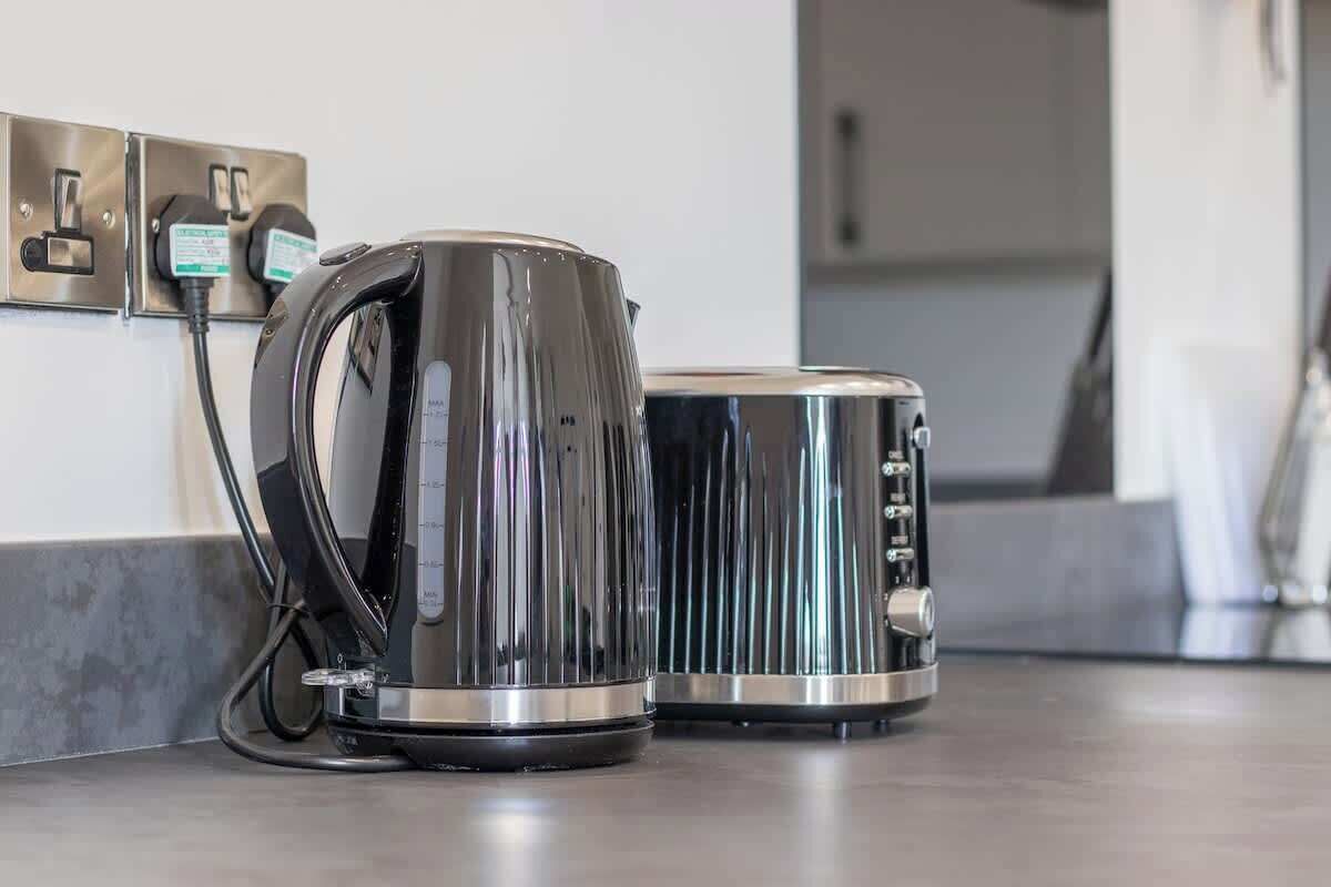A kitchen with a kettle and a toaster on a countertop, connected to a power outlet.