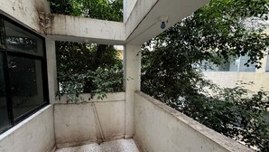 Un pequeño balcón cerrado con piso de concreto y paredes rodeadas de follaje.