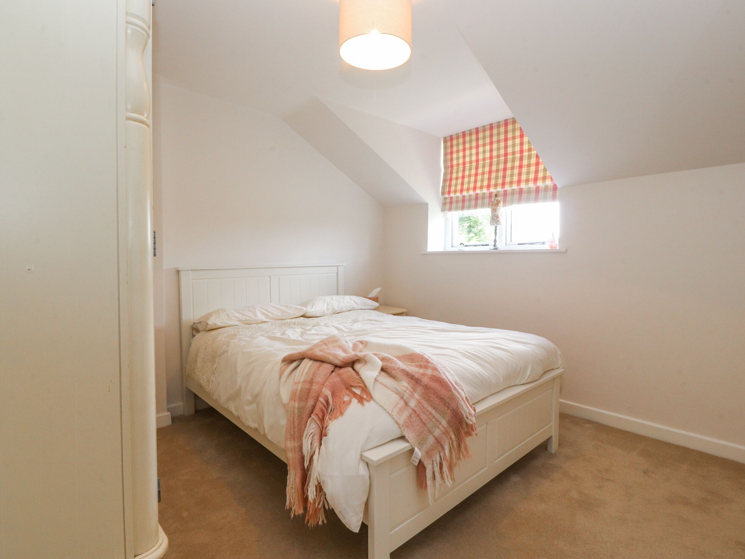 A bedroom with a bed, a window with a checkered valance, and a ceiling light fixture.
