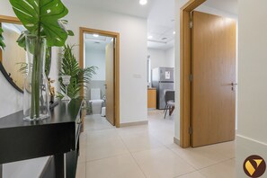 A hallway with a black console table, a mirror, and a potted plant. There is a wooden door on the right and a white door in the background leading to a kitchen area. - Vogue | Downtown near Dubai Mall | Burj Khalifa (Dubai)