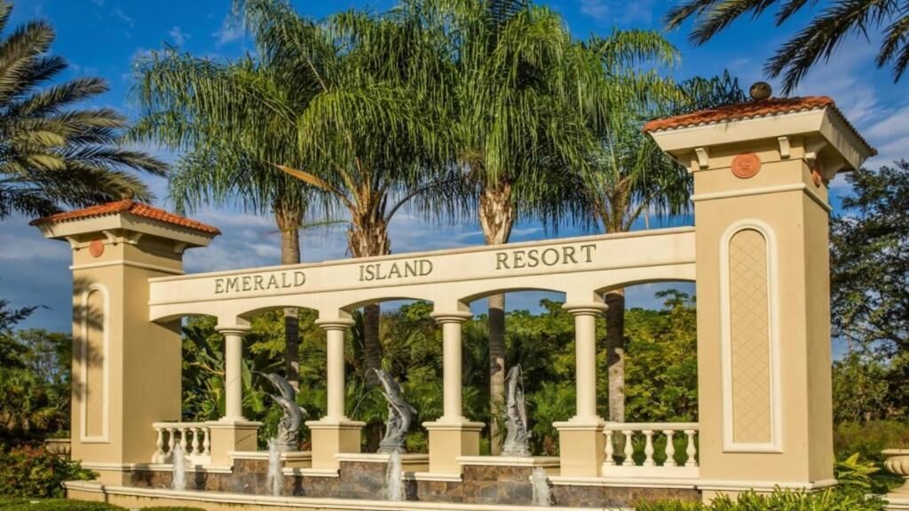 A sign for Emerald Island Resort with columns and a fountain.