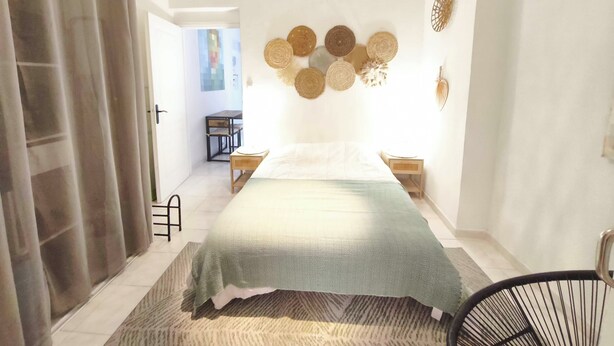 Un dormitorio con cama, mesitas de noche, una lámpara en la pared y una puerta.