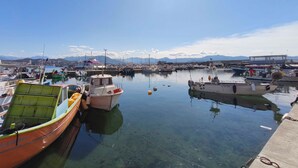 Una marina con varios barcos amarrados, agua cristalina y una cadena montañosa distante bajo un sol brillante.