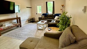 A living room with a sofa, a coffee table, a TV, and a plant. - Brand new 2BR, 1.5BA-close to amenities yet feels secluded. 2 story, AC, wifi! (Bridgton)