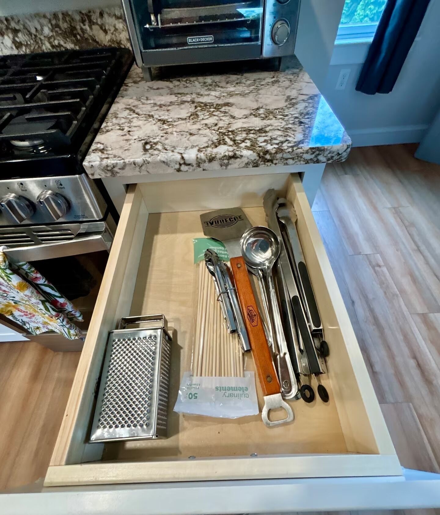 A kitchen drawer with a grater, measuring tools, and a TV.