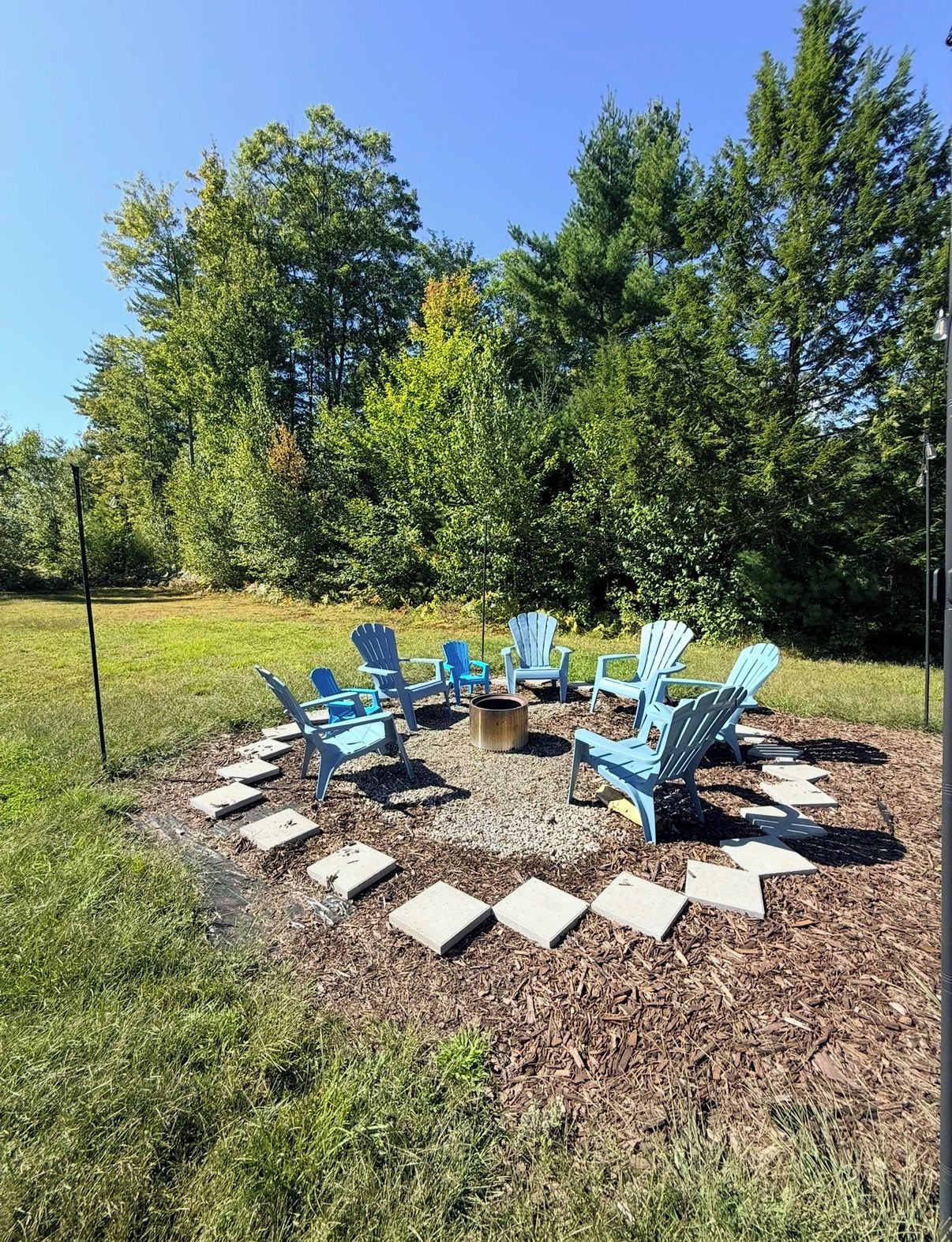 An outdoor seating area with Adirondack chairs arranged around a central fire pit, surrounded by a stone pathway.