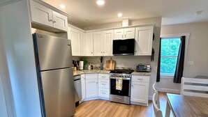 A modern kitchen with white cabinets, stainless steel appliances, and a wooden floor. - Brand new 2BR, 1.5BA-close to amenities yet feels secluded. 2 story, AC, wifi! (Bridgton)