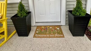 A white door with a window, two potted plants, and a welcome mat. - Brand new 2BR, 1.5BA-close to amenities yet feels secluded. 2 story, AC, wifi! (Bridgton)