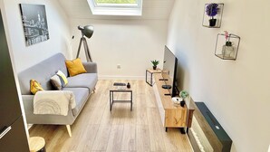 Ein modernes Wohnzimmer mit grauem Sofa, Holztisch und einem TV-Möbel mit Flachbildfernseher.