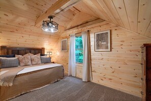 A cozy wooden cabin bedroom with a bed, curtains, and a ceiling light.
