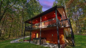 A two-story log cabin with a balcony, surrounded by a forest.