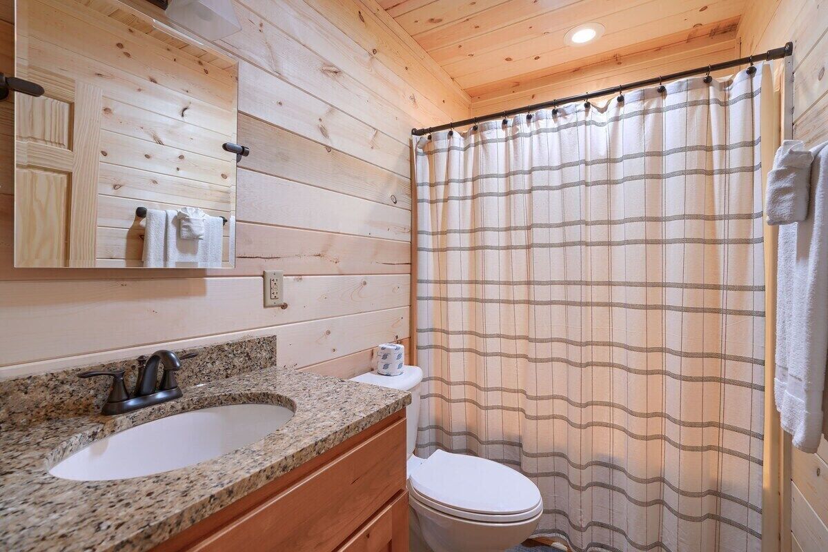 Een houten badkamer met een granieten wastafel, een wit toilet en een douchegordijn met strepen.