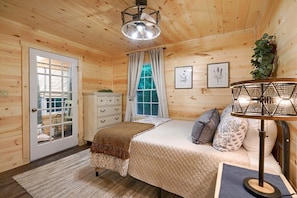 Quarto acolhedor de cabana de madeira, com cama, penteadeira e janela com cortinas.