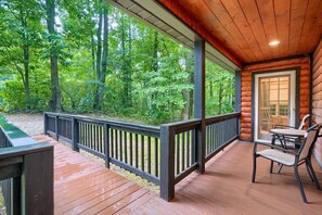 A wooden deck with a railing, a table with chairs, and a view of a forest.