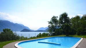 A rectangular swimming pool with a clear blue water surface, surrounded by a brick pathway, set against a backdrop of mountains and a lake. - View of Larian Triangle (Menaggio)
