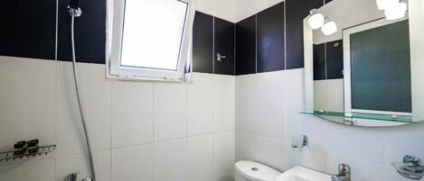A bathroom with a shower, toilet, sink, and a mirror with lights.