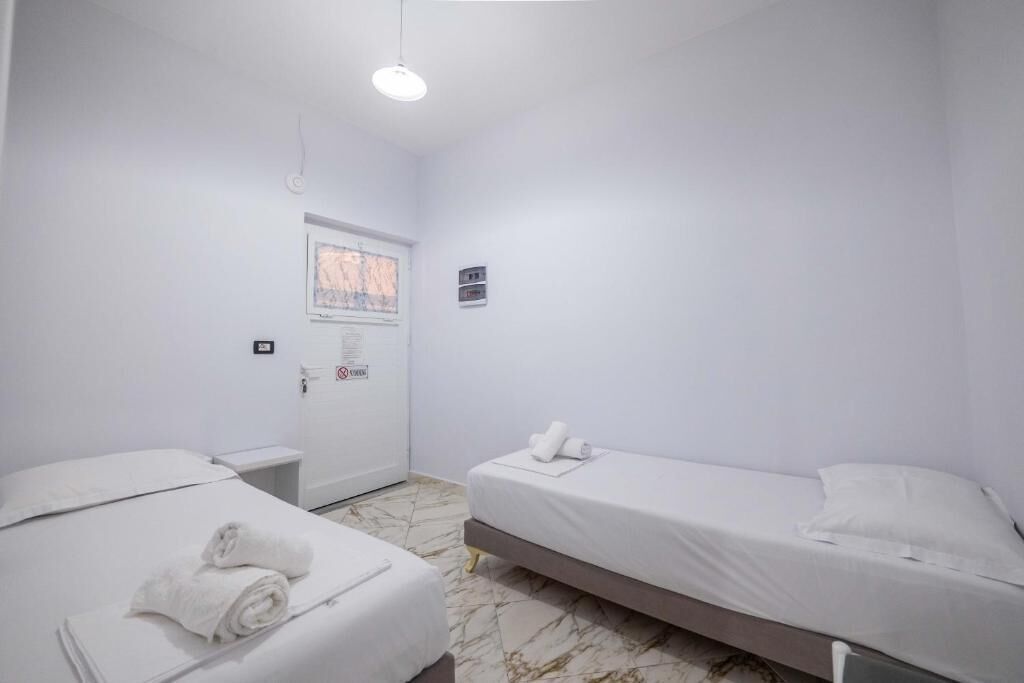 A clean, white room with two beds, a small window, and a door with a sign.