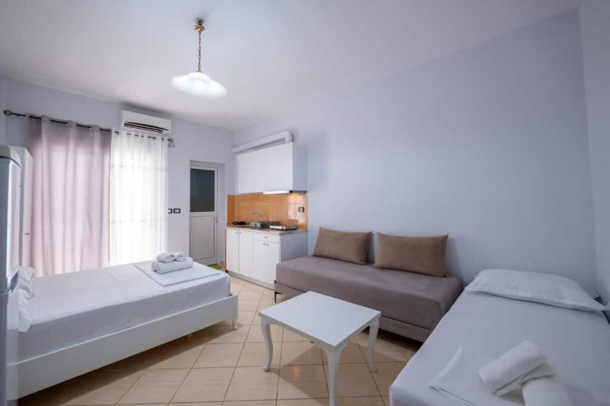 A hotel room with a bed, a sofa, a small table, a kitchenette, and a bathroom.