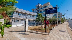 A modern villa with a stone pathway, a gated entrance, and a sign for 'Villa Nomia Apartments & Studios.' - Villa Nomia (Ksamil)