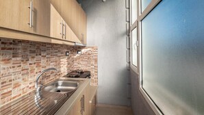 A compact kitchen with a tiled backsplash, a stainless steel sink, and wooden cabinets. - Villa Nomia (Ksamil)