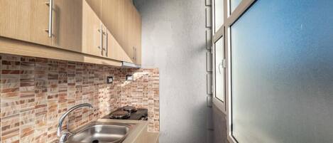 A compact kitchen with a tiled backsplash, a stainless steel sink, and wooden cabinets.