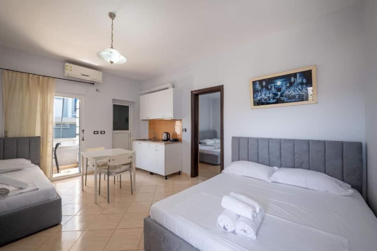 A hotel room with a bed, a desk, a kitchenette, and a balcony.