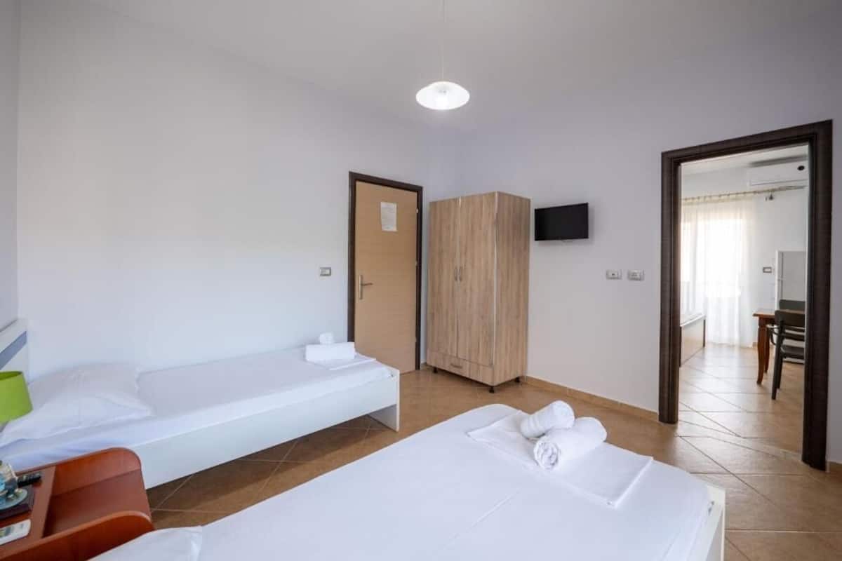 A hotel room with two single beds, a wooden wardrobe, a TV, and a bathroom visible through an open door.