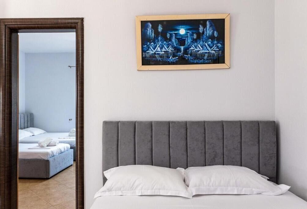 Un dormitorio con cabecera gris, cama con ropa de cama blanca y una obra de arte enmarcada en la pared.
