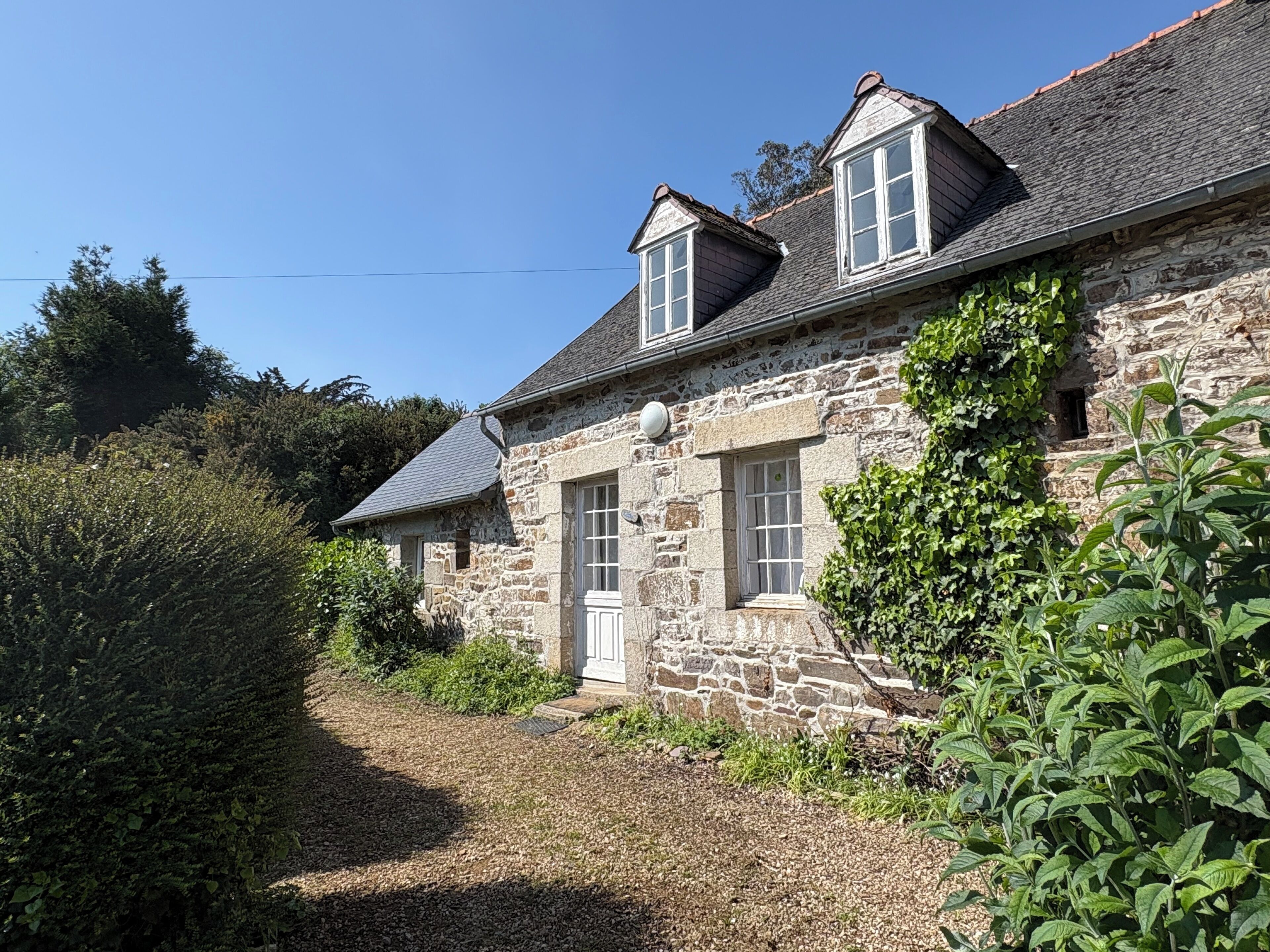 A stone house with a sloped roof, a small front porch, and a window with a white frame.