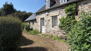 A stone house with a sloped roof, a small front porch, and a window with a white frame.