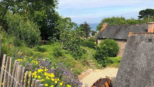 A garden with a wooden fence, a stone wall, and a view of the sea.
