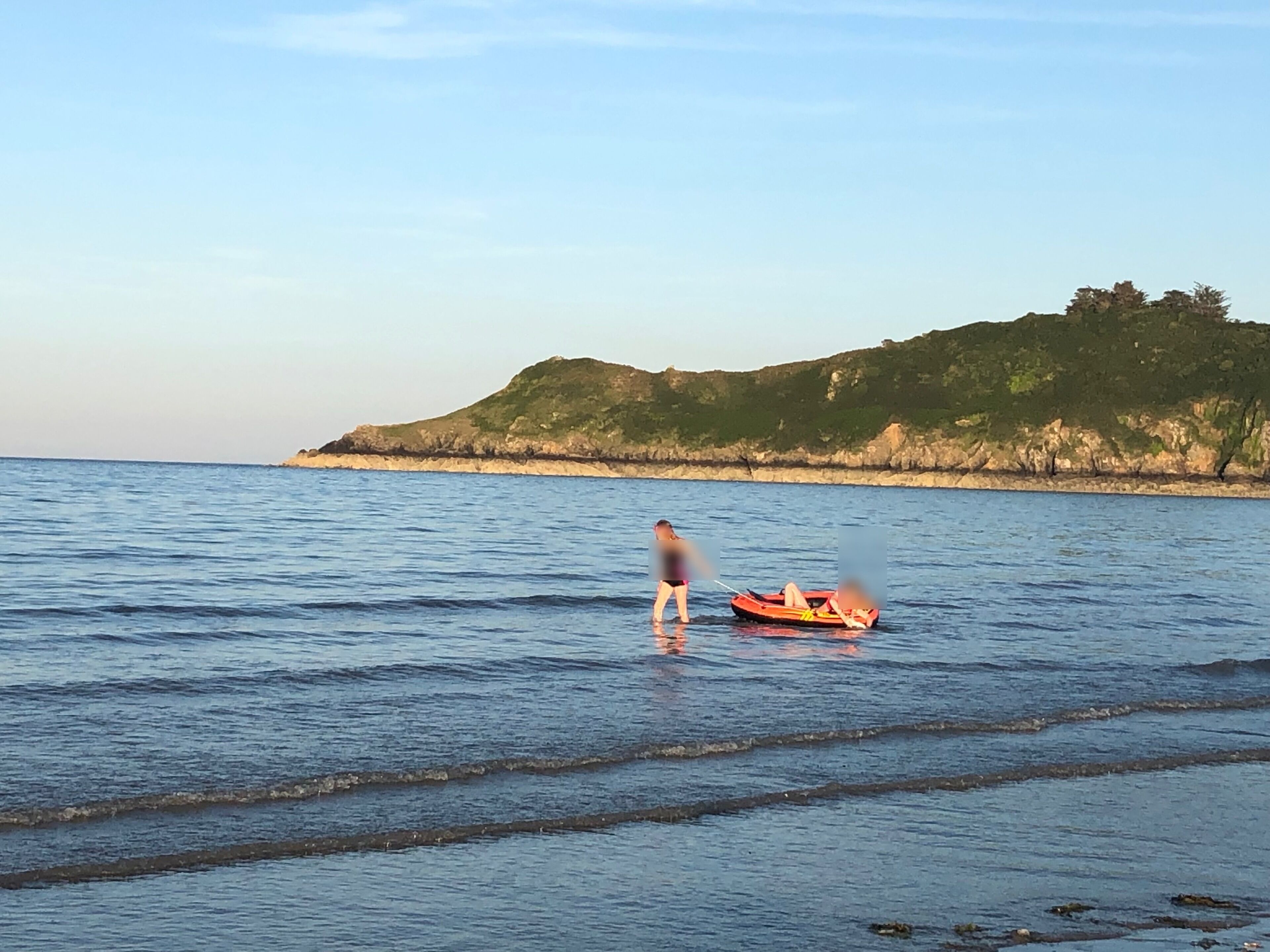 A calm sea with a small boat and a person standing on the shore.