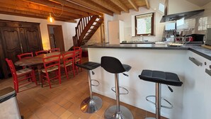 A kitchen with a wooden ceiling, a dining area with red chairs, and a bar with stools.