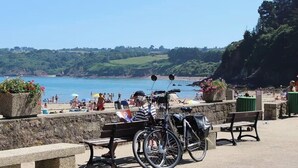 A coastal promenade with benches, a bicycle, and a view of the sea and greenery.