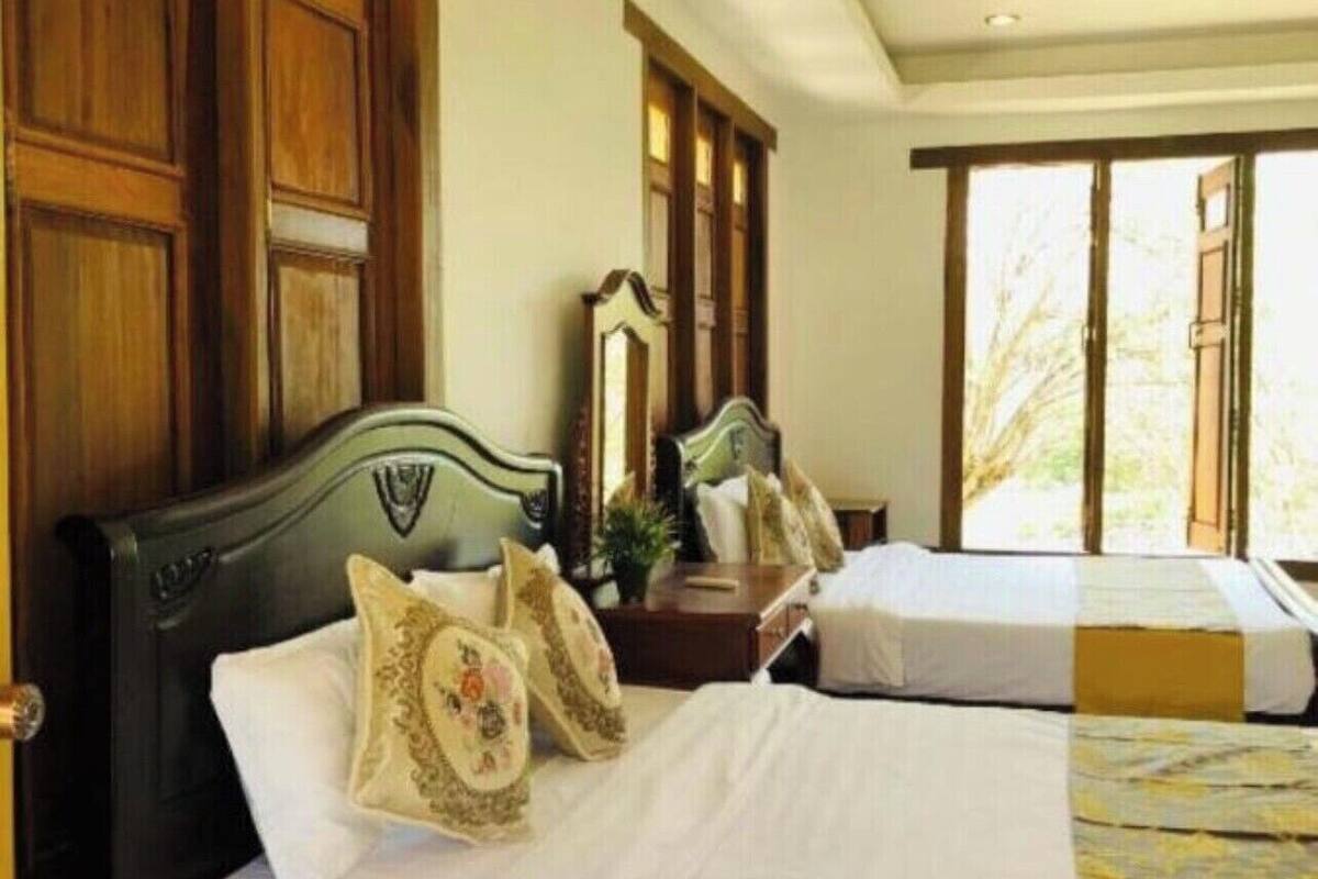A hotel room with two beds, wooden paneling, a large window, and a view of greenery outside.
