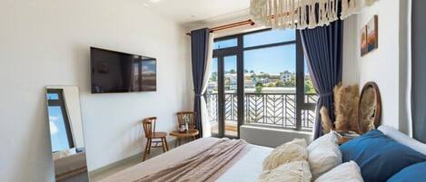 A hotel room with a bed, a TV, a balcony with a view, and a hanging light fixture.