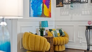 A room with a white wall, a colorful abstract painting, a patterned lamp, and a wooden side table with a vase and a plant. - Spacious Atlanta Home – Sleeps 10, Kid-Friendly + Big Porch & Yard (Atlanta)