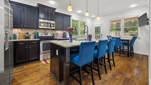 A modern kitchen with dark cabinets, stainless steel appliances, and blue bar stools. - Spacious Atlanta Home – Sleeps 10, Kid-Friendly + Big Porch & Yard (Atlanta)