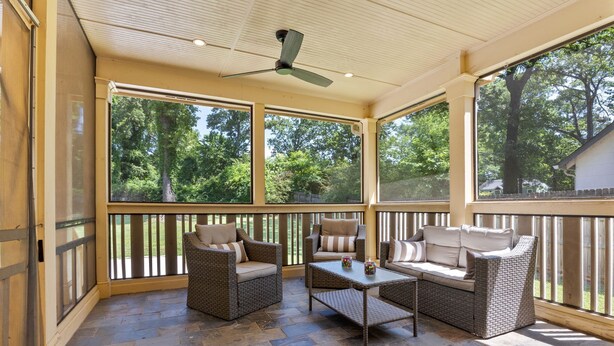 A covered patio with wicker furniture, a table, and large windows overlooking a wooded area. - Spacious Atlanta Home – Sleeps 10, Kid-Friendly + Big Porch & Yard (Atlanta)