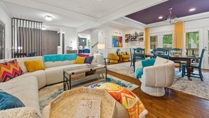 A spacious living room with a sectional sofa, a white armchair, and a dining area with a table and chairs. - Spacious Atlanta Home – Sleeps 10, Kid-Friendly + Big Porch & Yard (Atlanta)