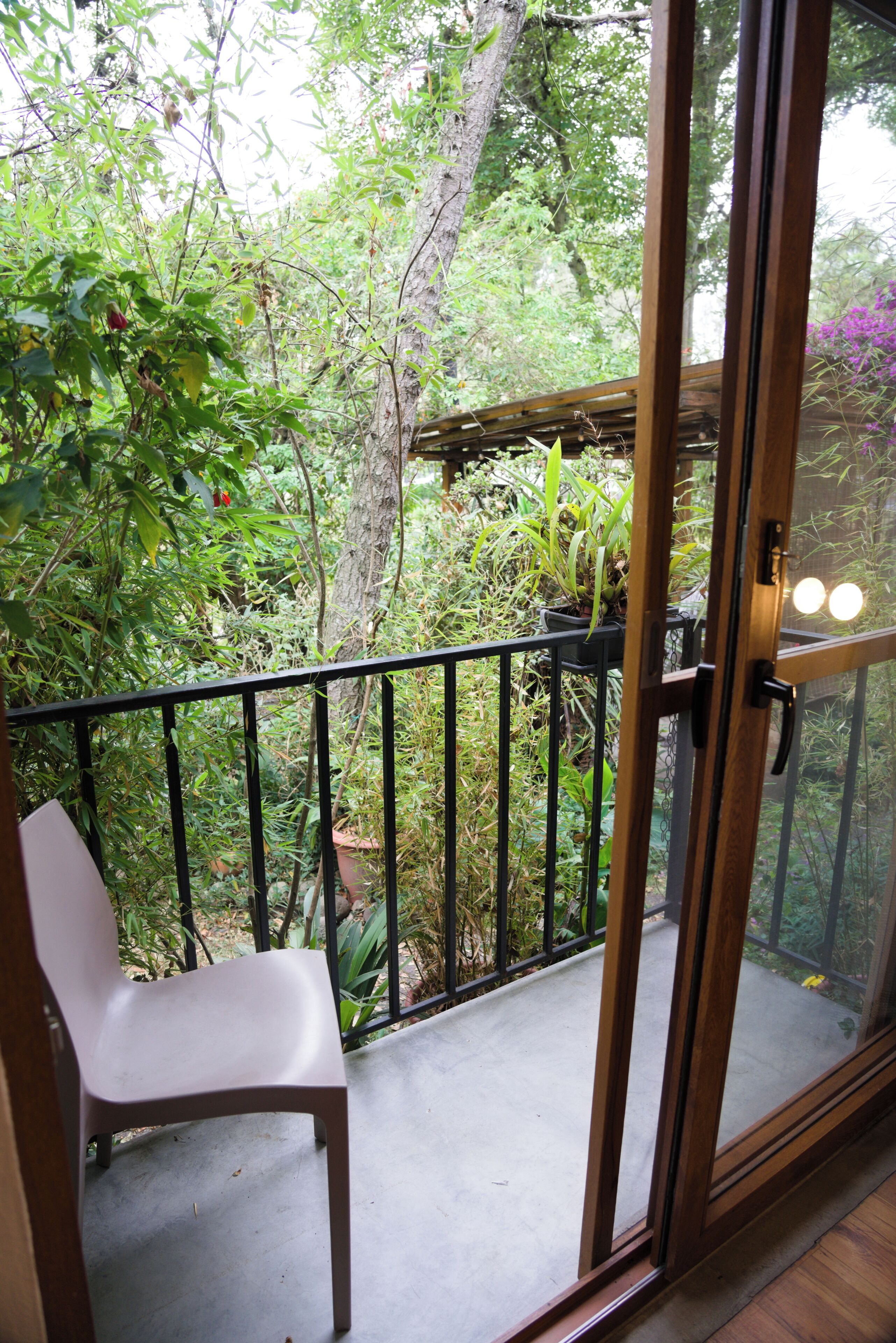 Een balkon met een stoel, een bloempot en uitzicht op weelderige begroeiing.
