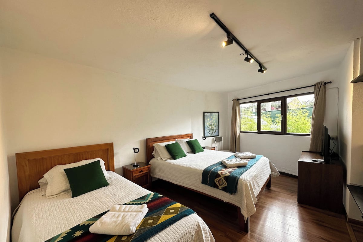 Habitación de hotel con dos camas, ventana con vistas, escritorio con televisor y lámpara en el techo.