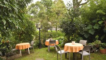 Une terrasse de jardin agrémentée de tables et de chaises, entourée d’une végétation luxuriante et d’arbres.