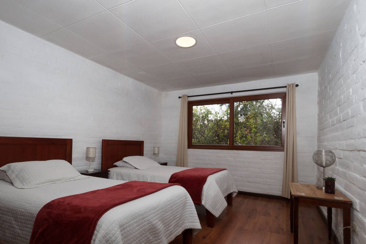 Una habitación con dos camas, una ventana, una mesa y una lámpara en el techo.