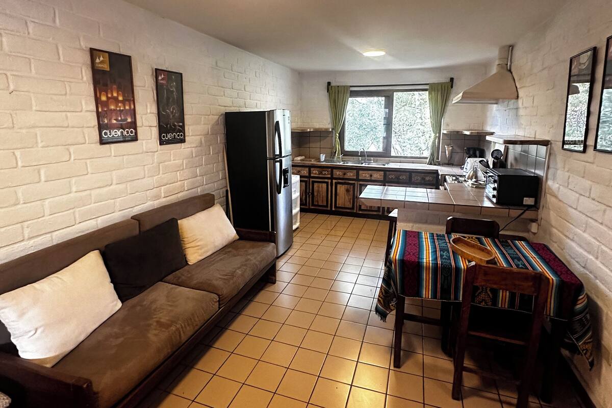 Un espacio habitable compacto con sofá, una mesa de comedor con sillas, una zona de cocina con fregadero y estufa, y un refrigerador.