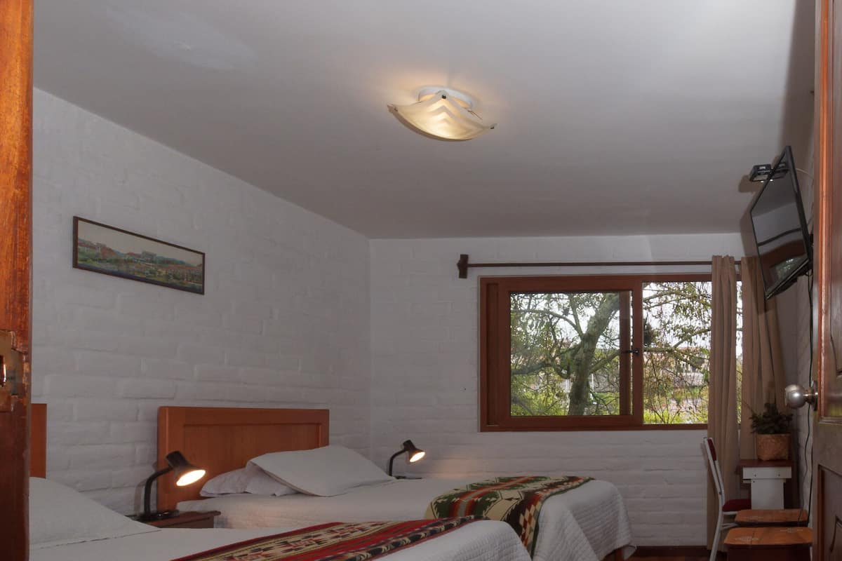 Una habitación con dos camas, piso de madera, ventana con vistas y televisión montada en la pared.