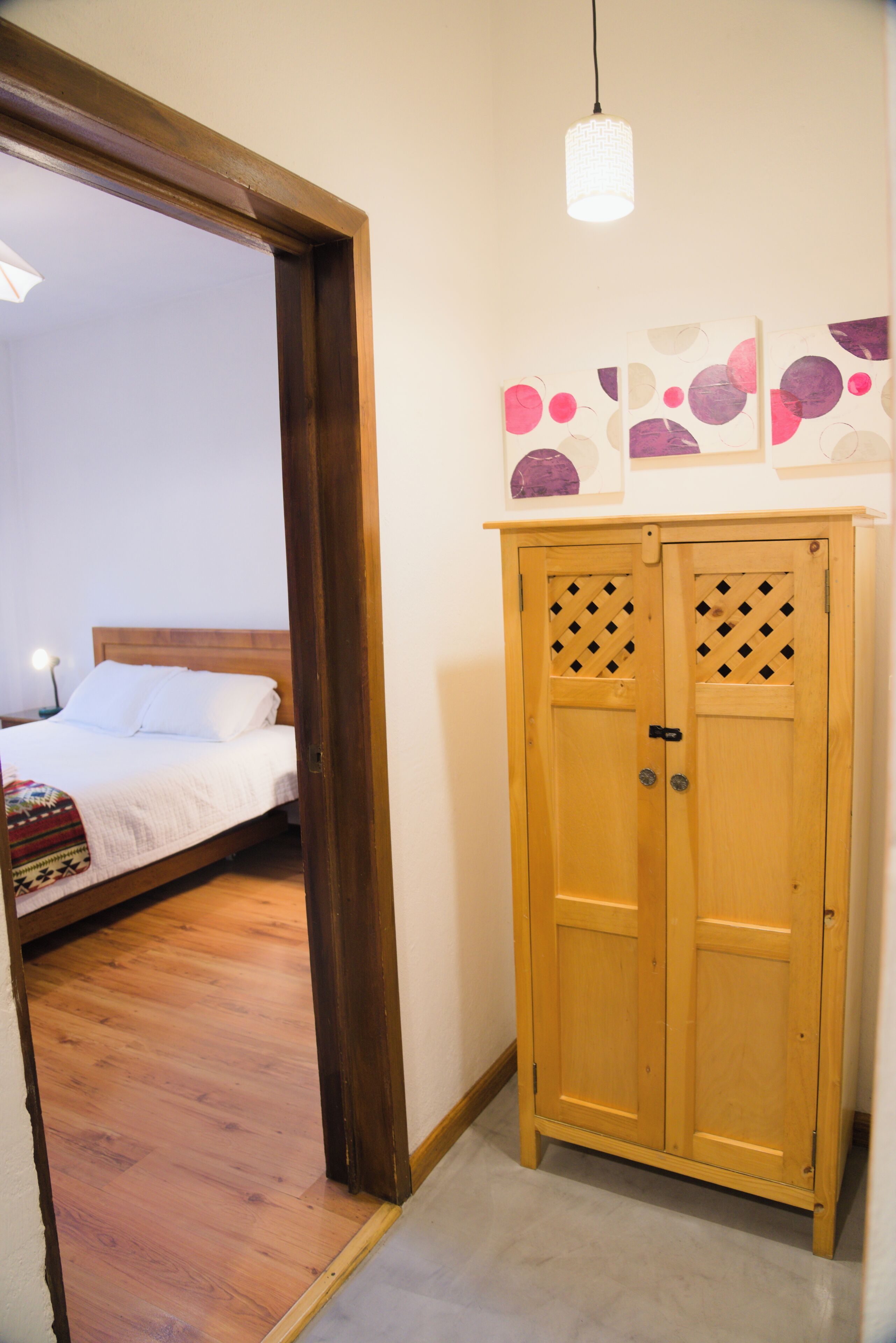 Une pièce avec une armoire en bois, un lit avec une literie blanche et un luminaire suspendu.