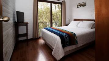 A bedroom with a bed, a TV on a small table, a window with curtains, and a picture on the wall.
