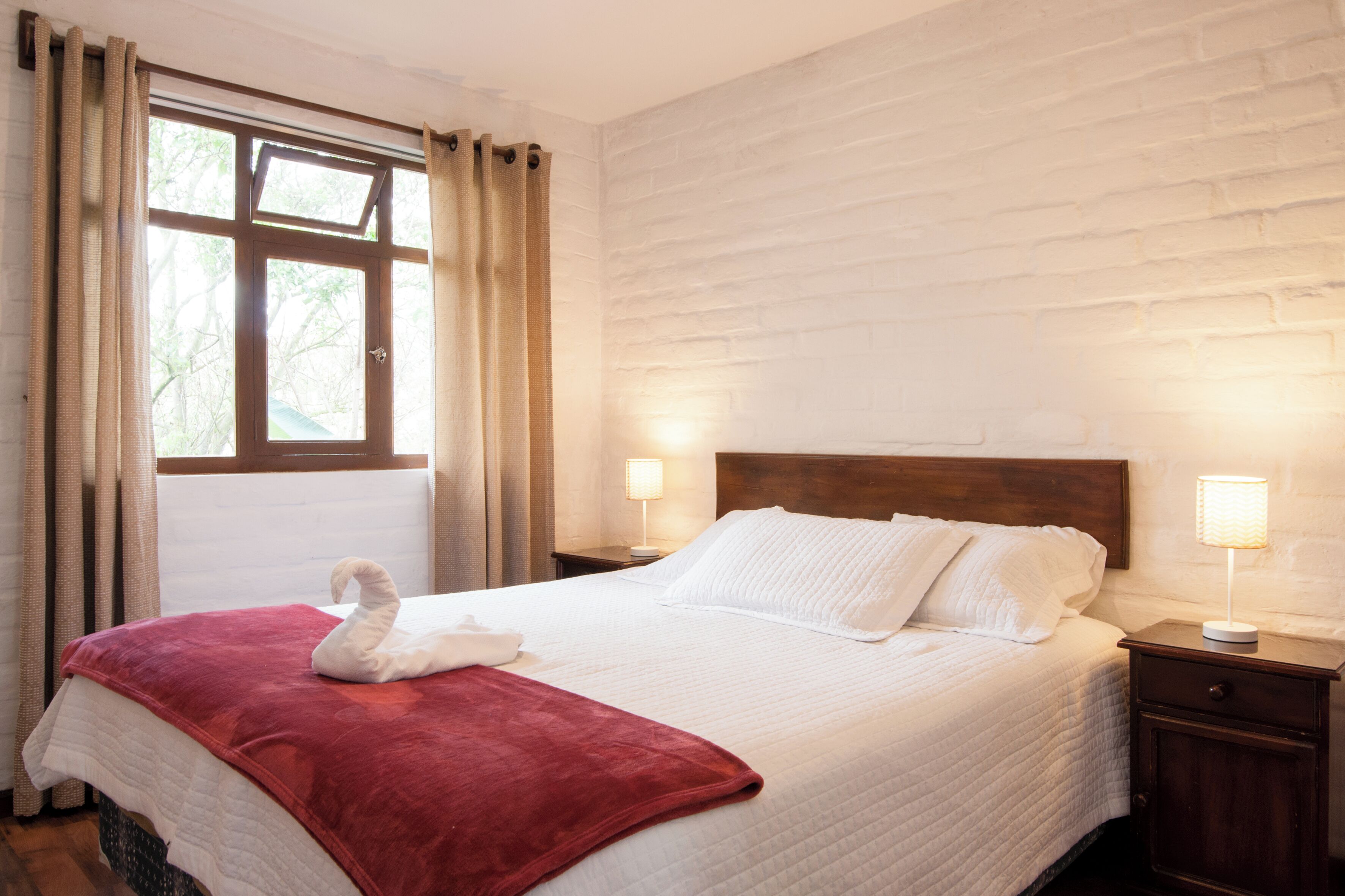 A neatly made bed with a red blanket, a wooden headboard, and two bedside lamps.