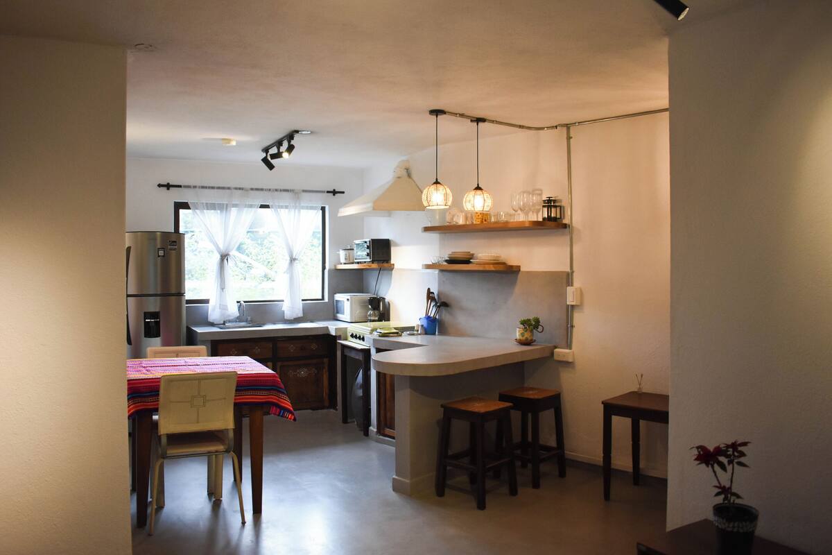 Una cocina compacta con una isla central, taburetes de bar y un comedor con mesa y sillas.